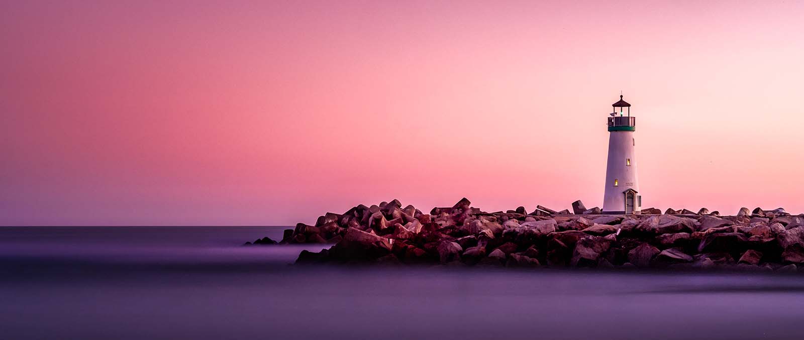 pink and orange sky with lighthouse on land near the ocean