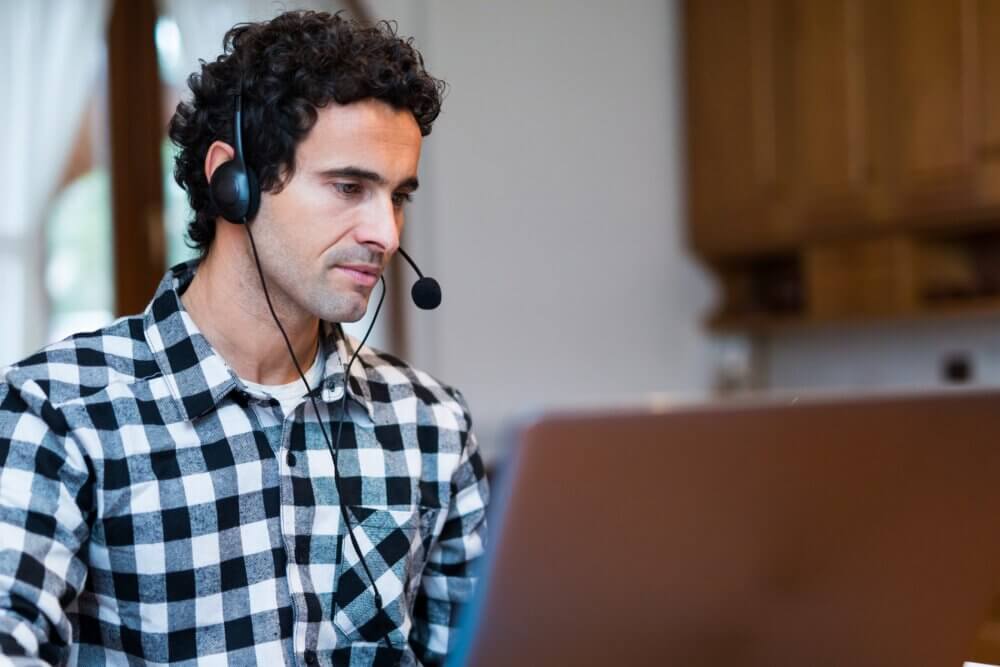 Man with plaid shirt on wearing a headset while talking on a computer call