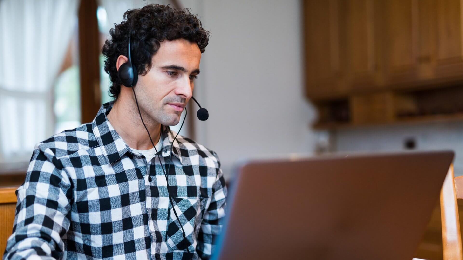 Man with plaid shirt on wearing a headset while talking on a computer call