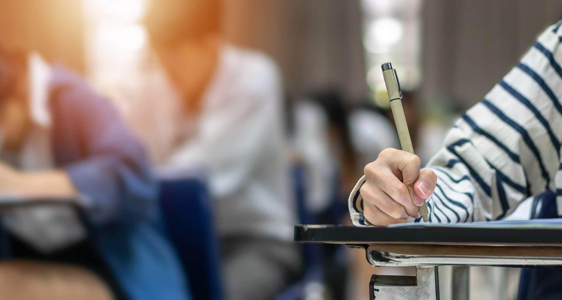 Students writing with pen, filling out an exam