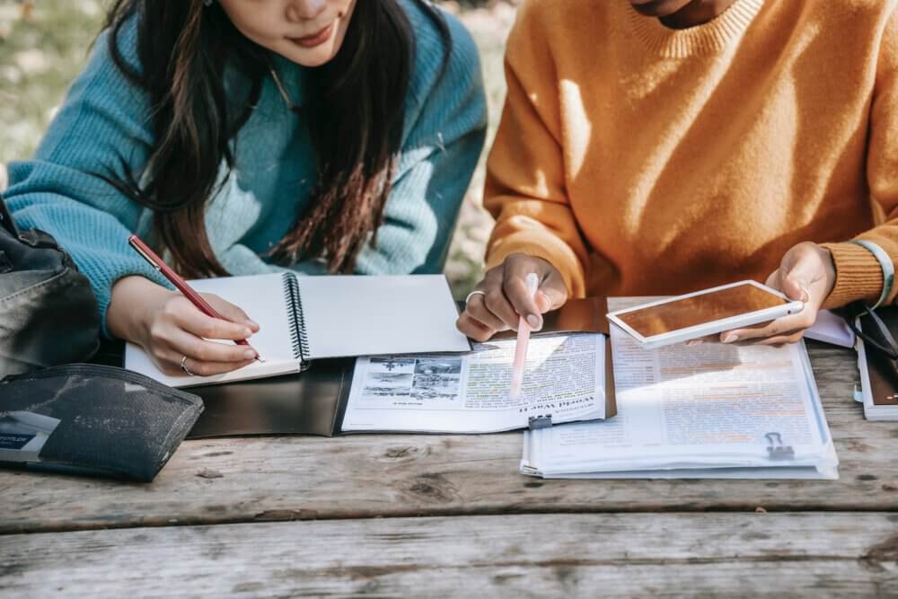two women in blue and white sweaters comparing notes on paper