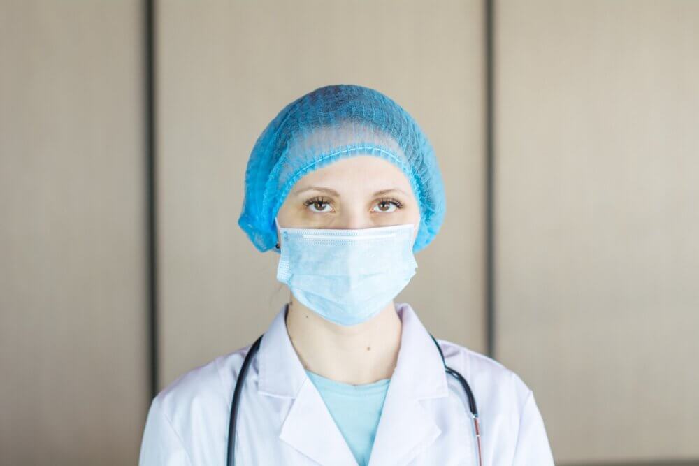 Nurse in white lab coat, blue face mask, and hair cap