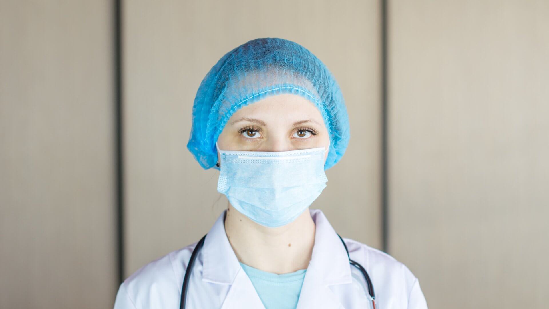 Nurse in white lab coat, blue face mask, and hair cap