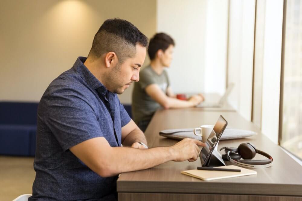 Man wearing blue collared shirt writing on iPad while standing