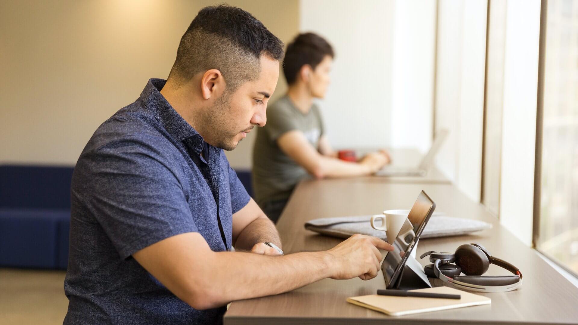 Man wearing blue collared shirt writing on iPad while standing