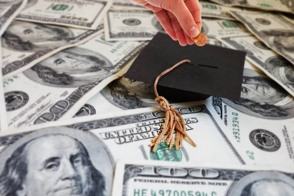 Hand putting money into a graduation cap -- student loan repayment or college savings concept