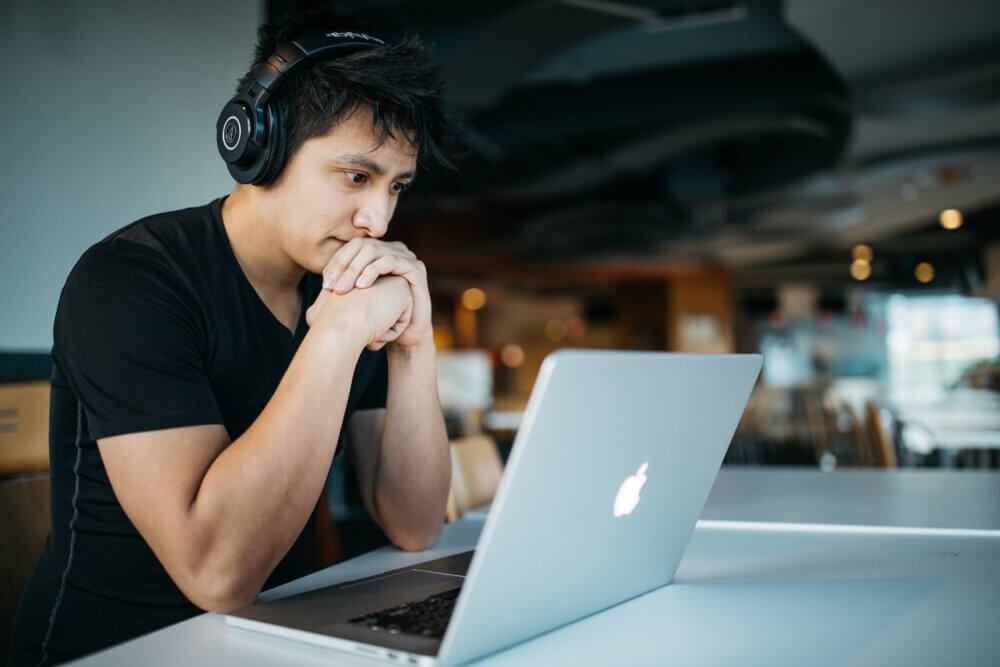 Frustrated student sitting at desk with open Mackbook and headphones on