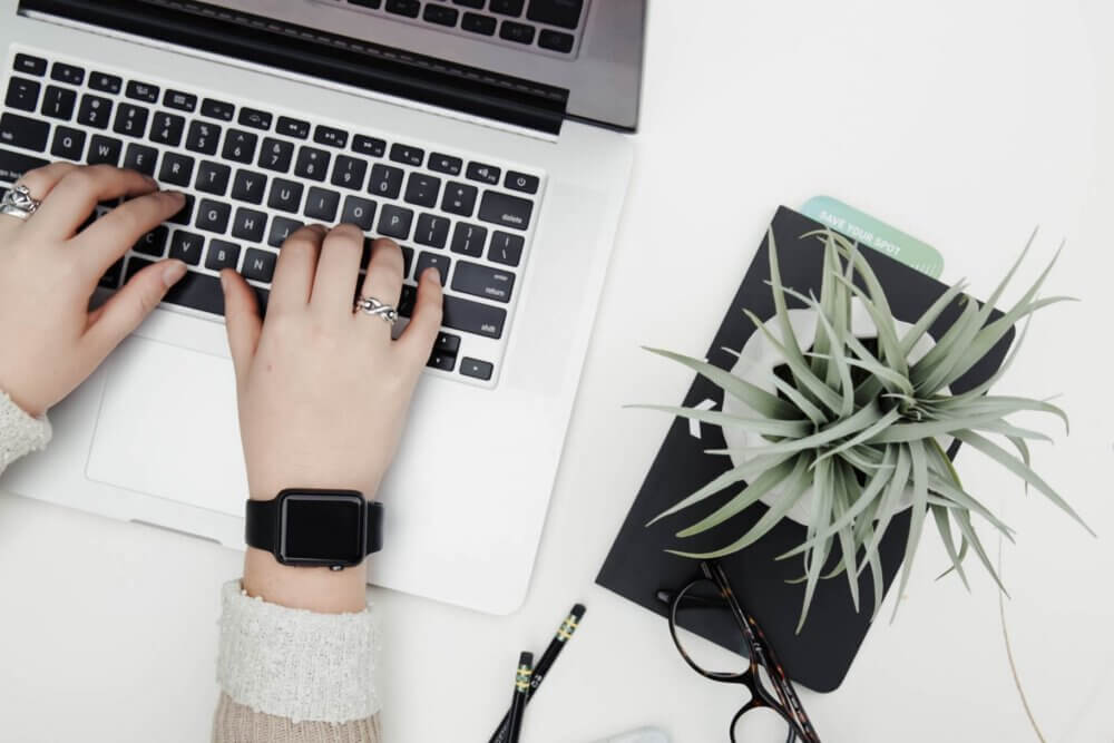 woman typing on Macbook seated at white table