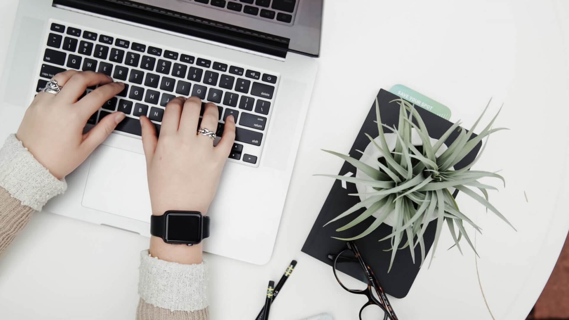 woman typing on Macbook seated at white table