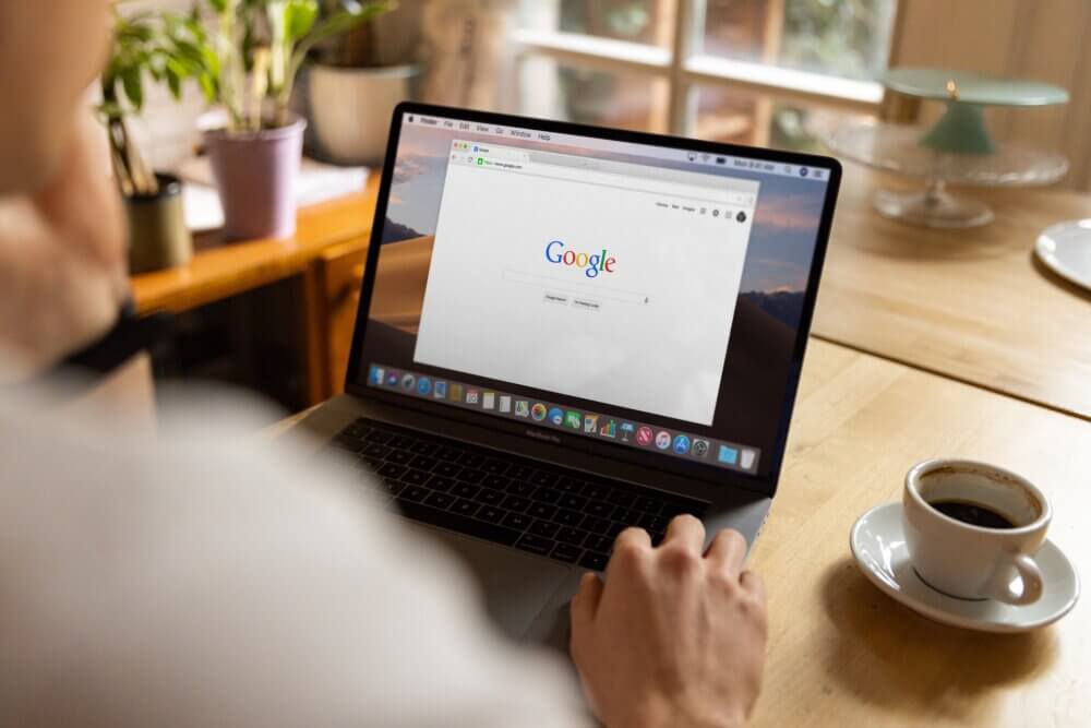 person typing into Google on Macbook while drinking coffee