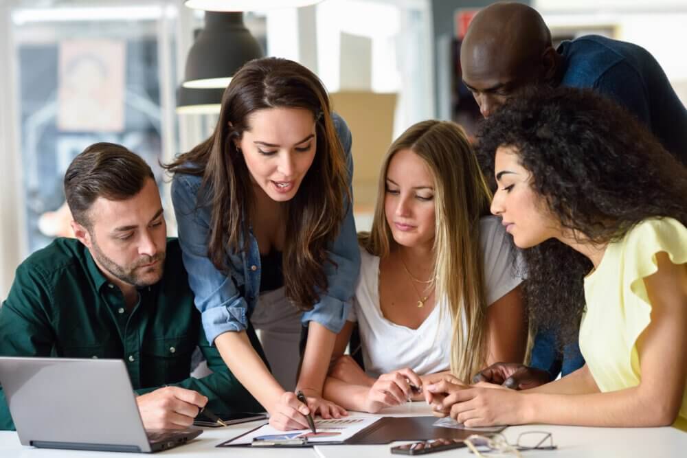 Five young people studying on white desk. Women and men working together wearing casual clothes. Multi-ethnic group.