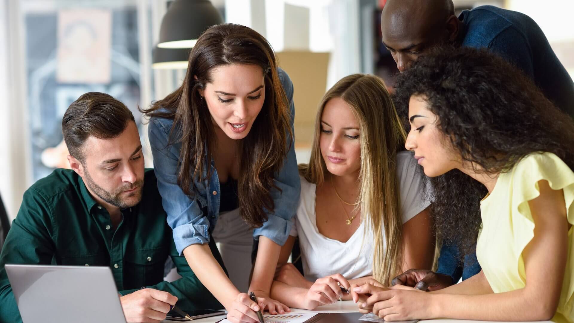 Five young people studying on white desk. Women and men working together wearing casual clothes. Multi-ethnic group.