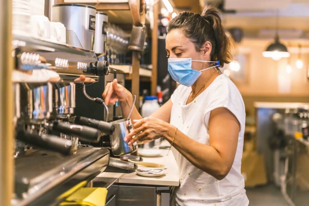 woman in mask makes coffee on campus