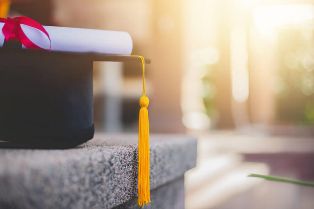 Close-up focus of university graduates placing a bachelor's certificate and a commemorative cap at the graduation ceremony. Success, celebration