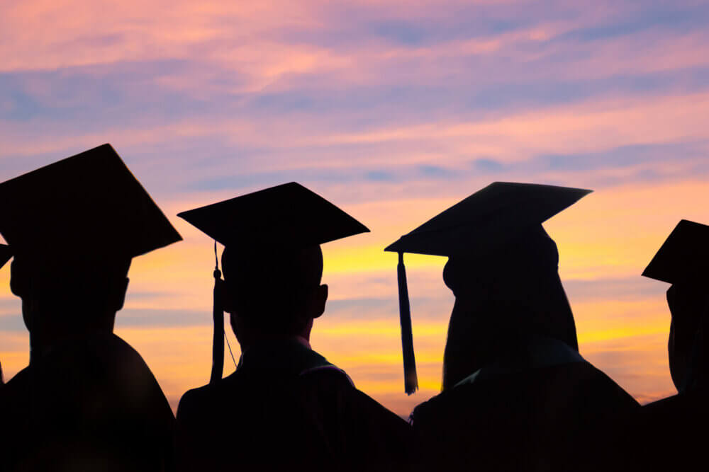 Silhouettes of students with graduate caps in a row on sunset background. Graduation ceremony at university web banner.