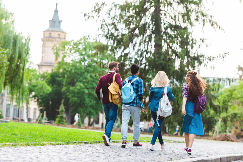 back view of students with backpacks walking on street