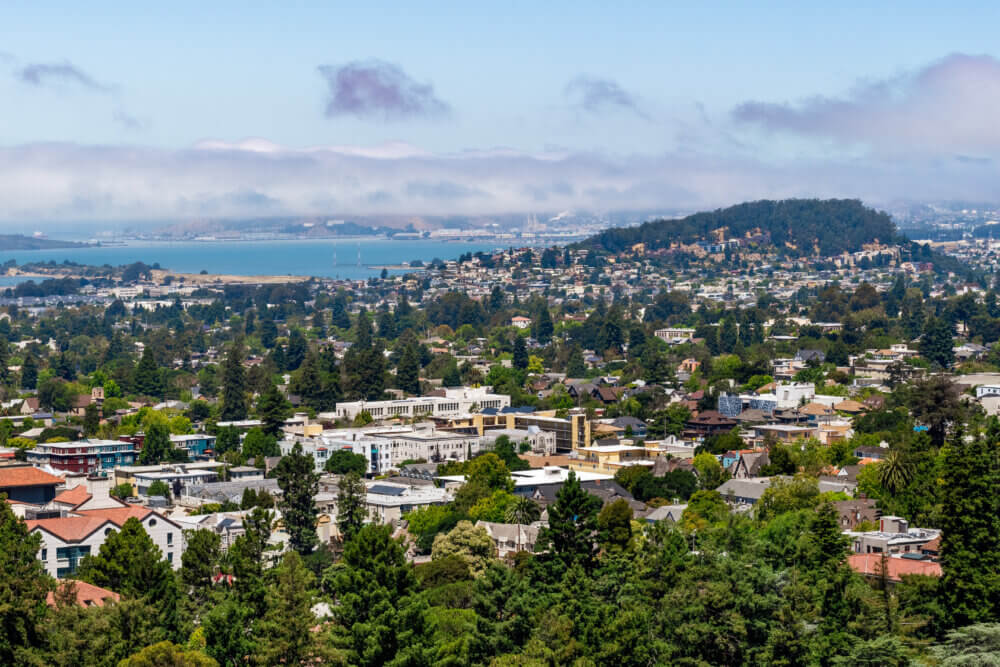 View towards Berkeley, Richmond and the San Francisco bay area shoreline on a sunny day; University of California Berkeley campus buildings in the foreground, California