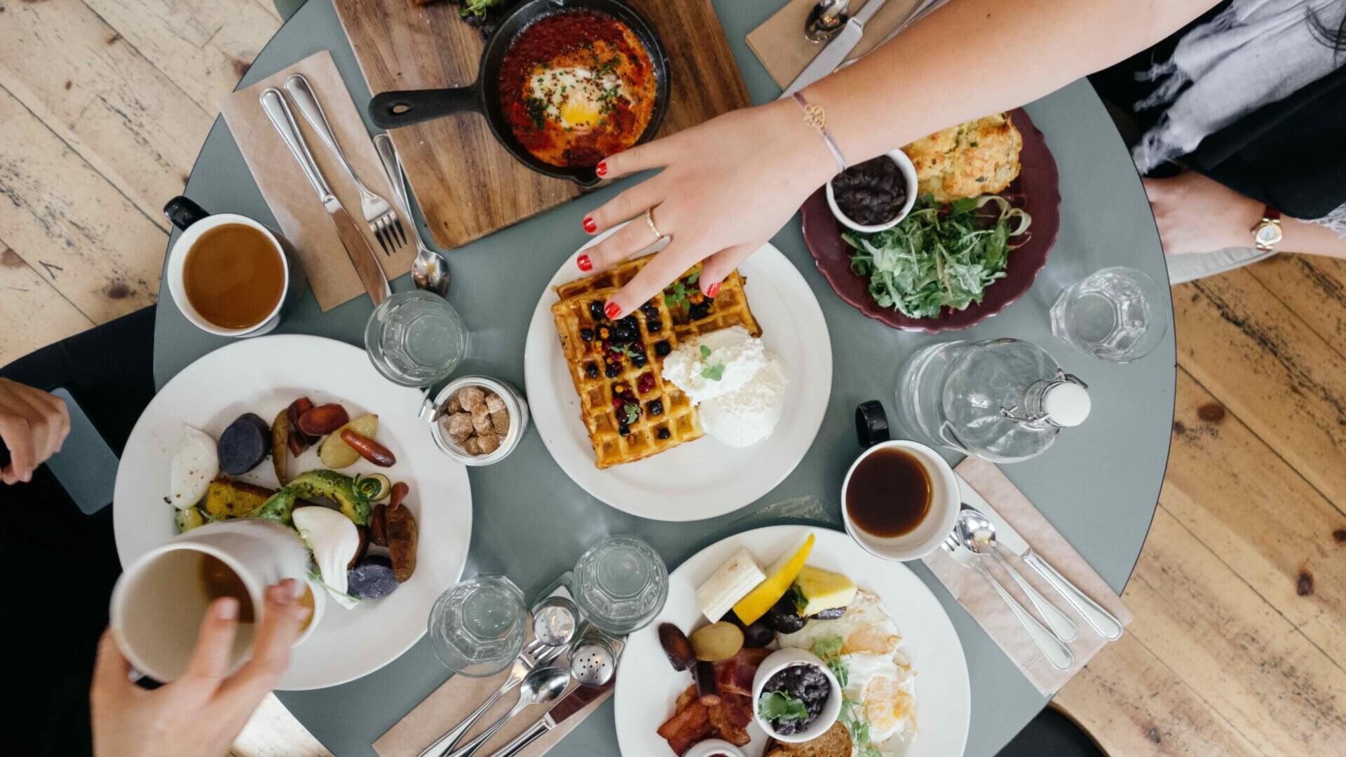 a hand reaches for a waffle on a table full of food
