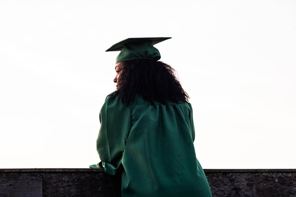 Woman standing against a wall in graduation gown and cap