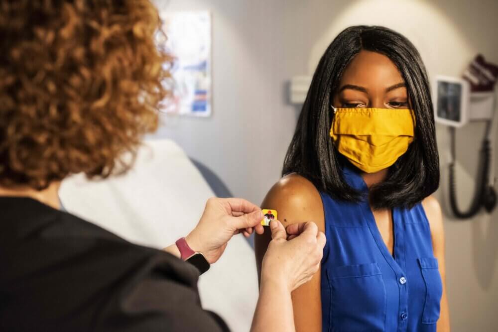 a nurse puts a bandaid of the arm of a new vaccinated college student