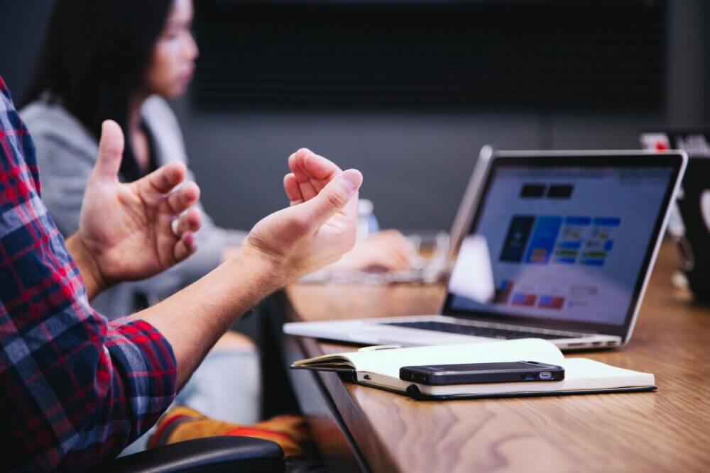 man talking and explaining with his hands while sitting in front of a computer
