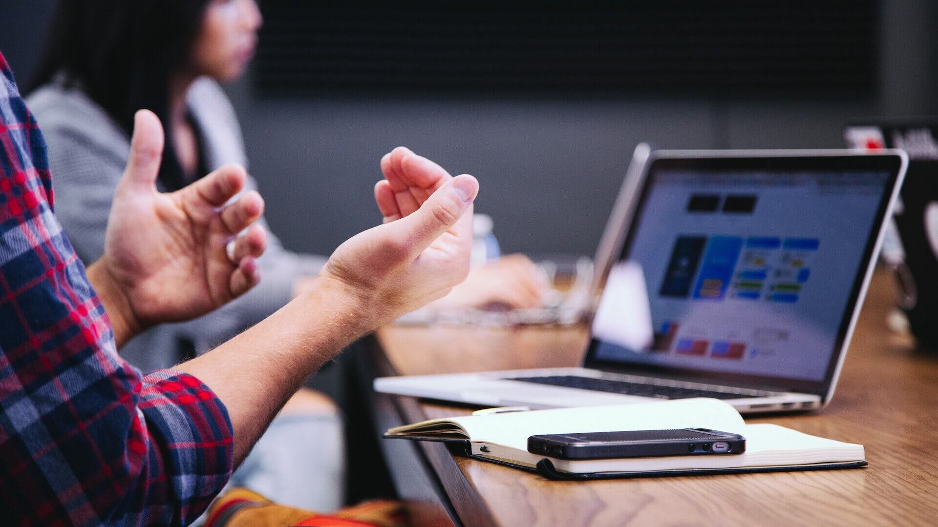man talking and explaining with his hands while sitting in front of a computer