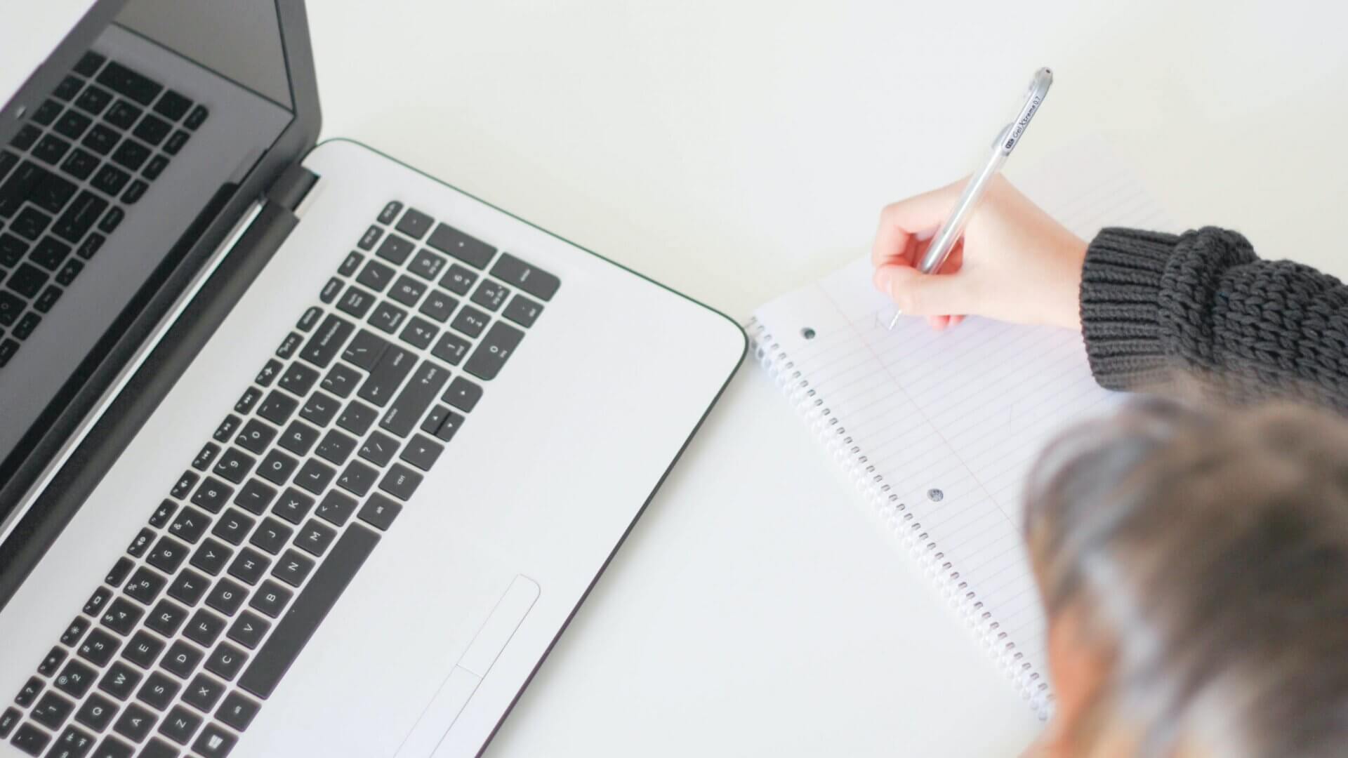 woman writing on a notepad with laptop in front