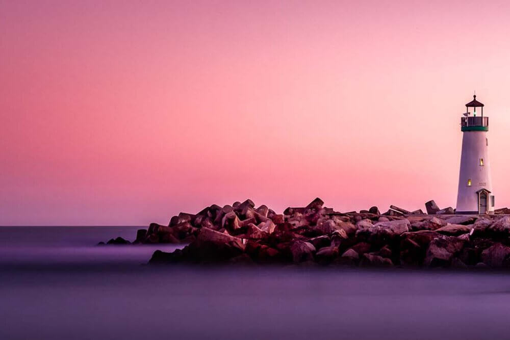 pink and orange sky with lighthouse on land near the ocean