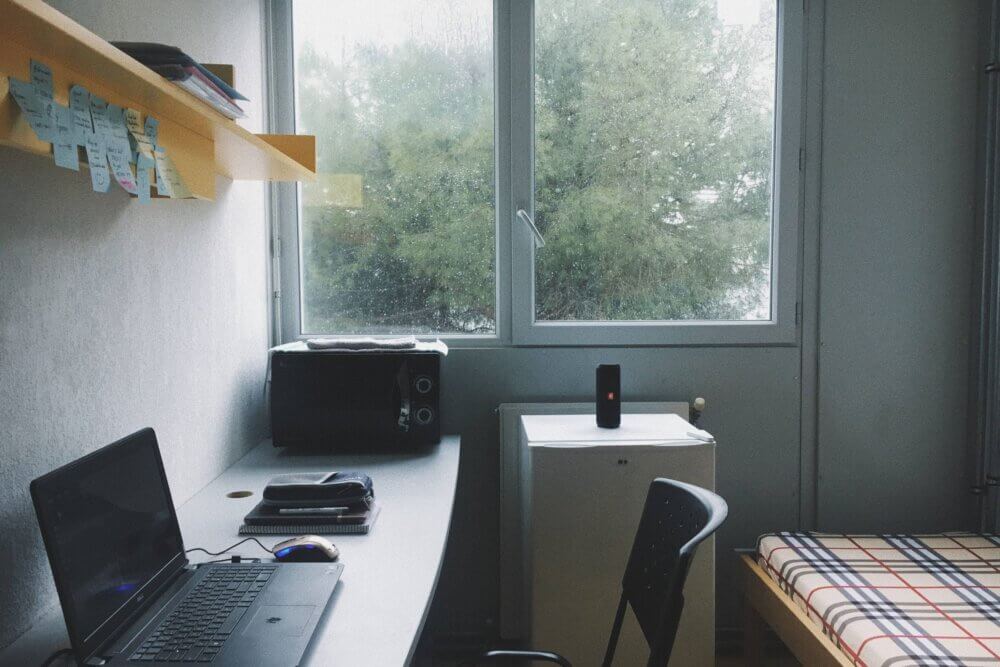a sparsely decorated dorm room with bed, desk, microwave and mini fridge