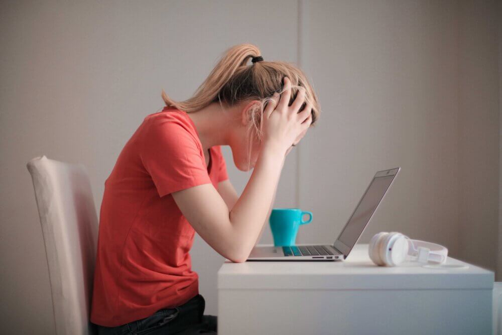 a student looks down at her laptop with her hands on her head