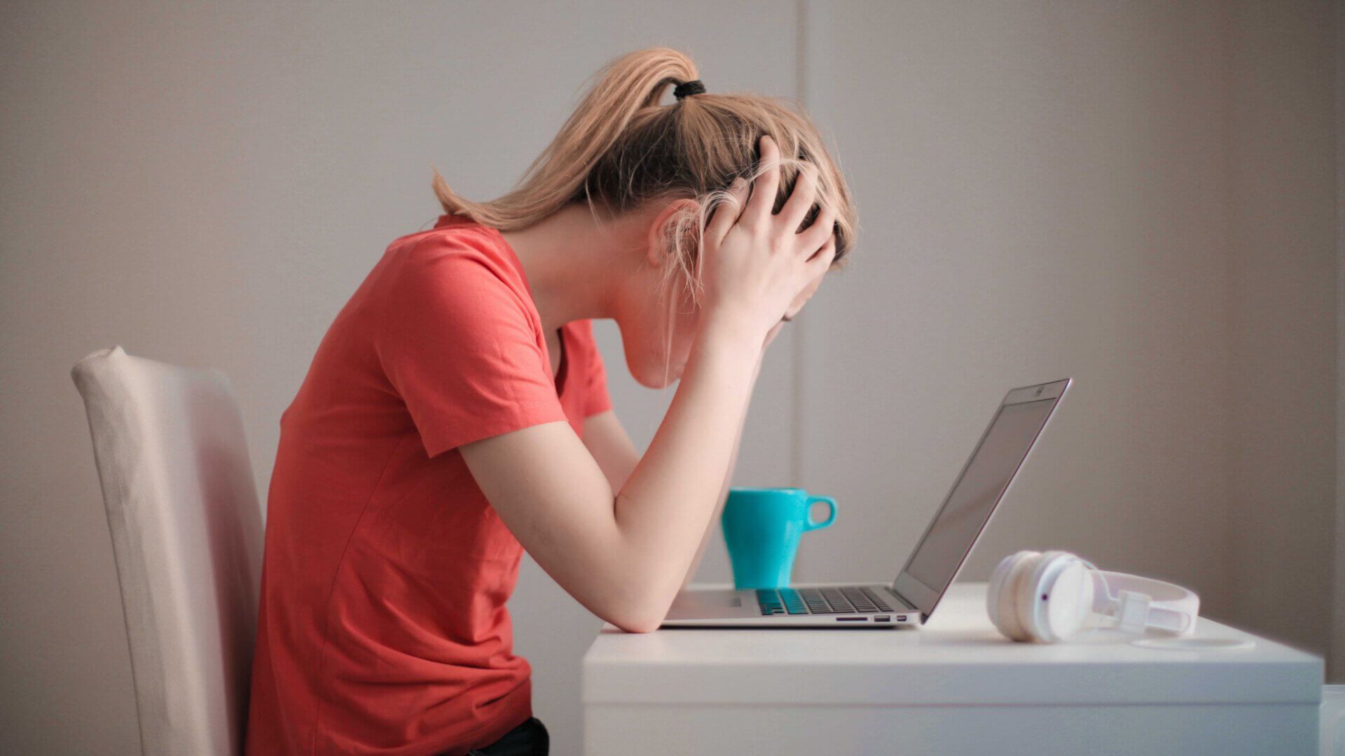 a student looks down at her laptop with her hands on her head