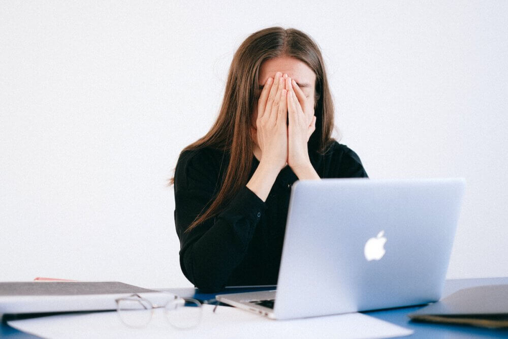a student covers her face while looking at a laptop