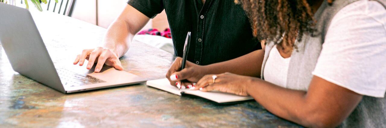 man and woman working on computer and writing notes