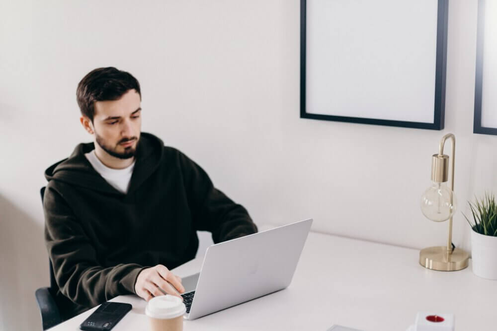 Man looking at computer screen with coffee and phone
