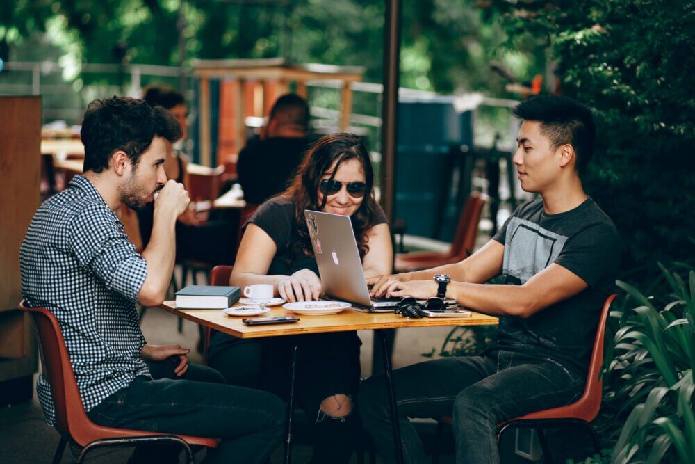 Three people working outdoors on a laptop