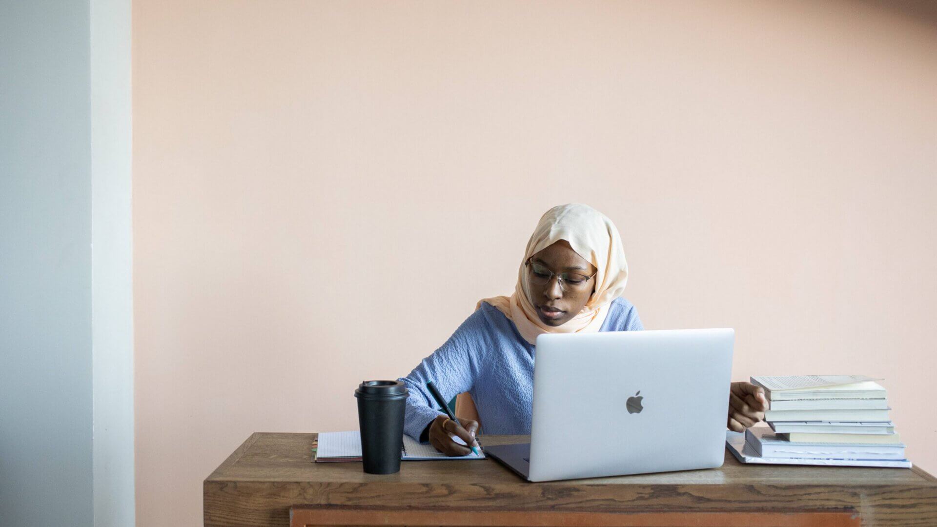 a woman writes in a notebook next to her open laptop