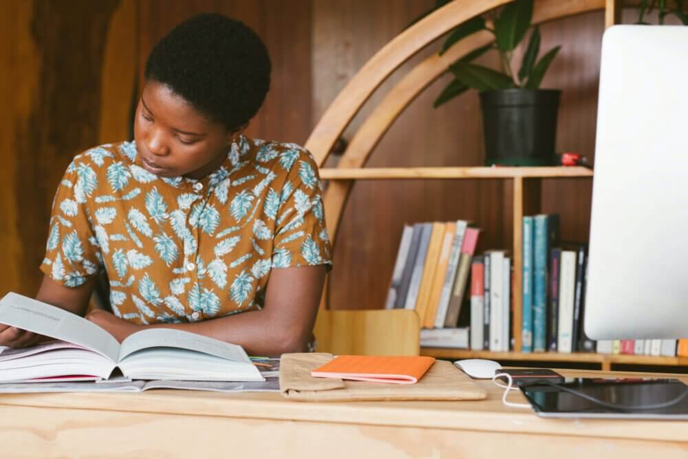 a female college student looks through a textbook while sitting at a desk.