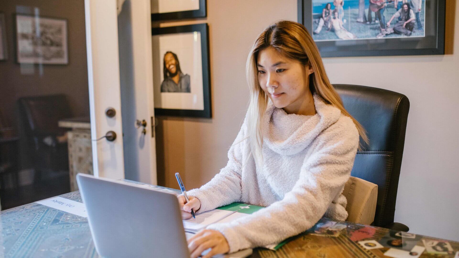 A teen girl staring intently at her laptop while taking notes during an online class
