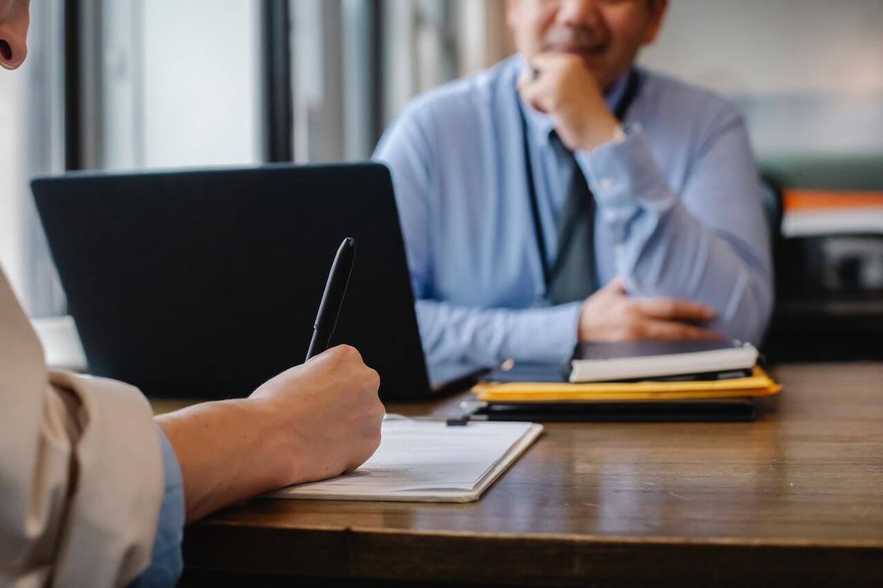 Person taking notes across desk from man