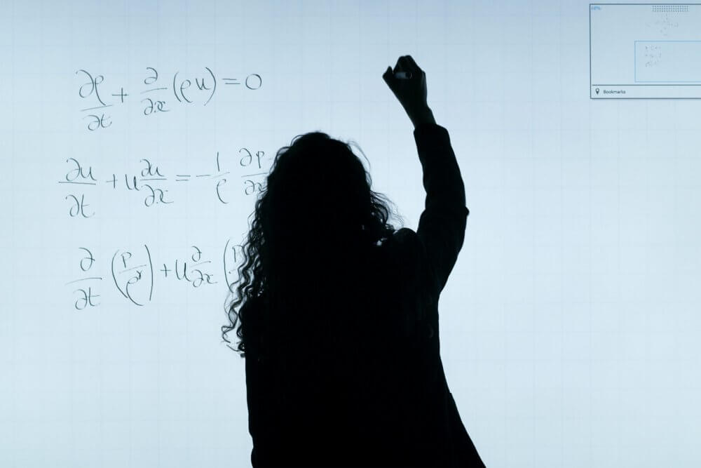 a professor writes an engineering equation on the white board