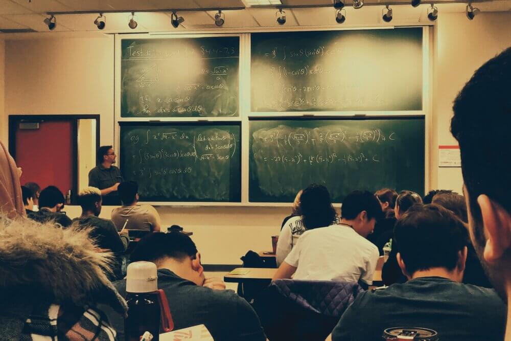 students sitting on chairs in front of chalkboard in classroom