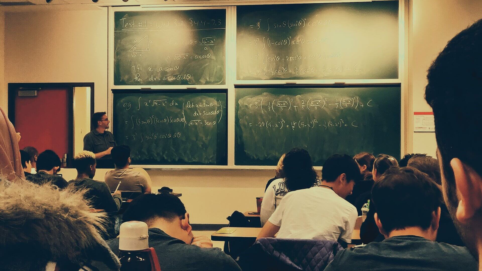 students sitting on chairs in front of chalkboard in classroom