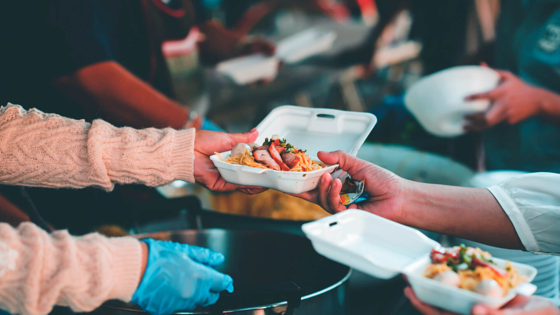 Person serving food in a white box to another person in hunger