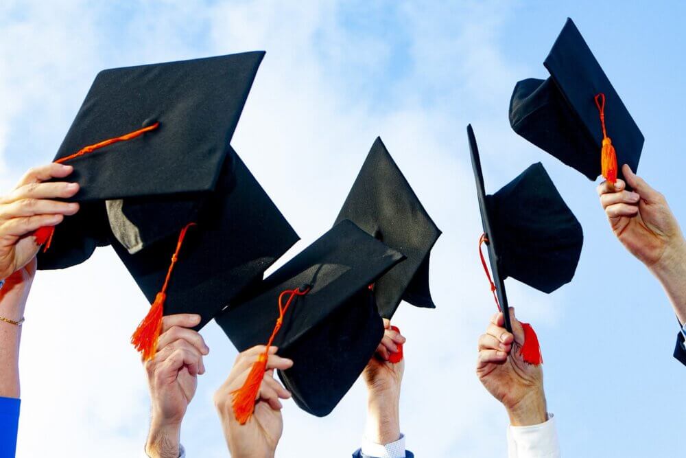 six people holding black graduation caps in the air