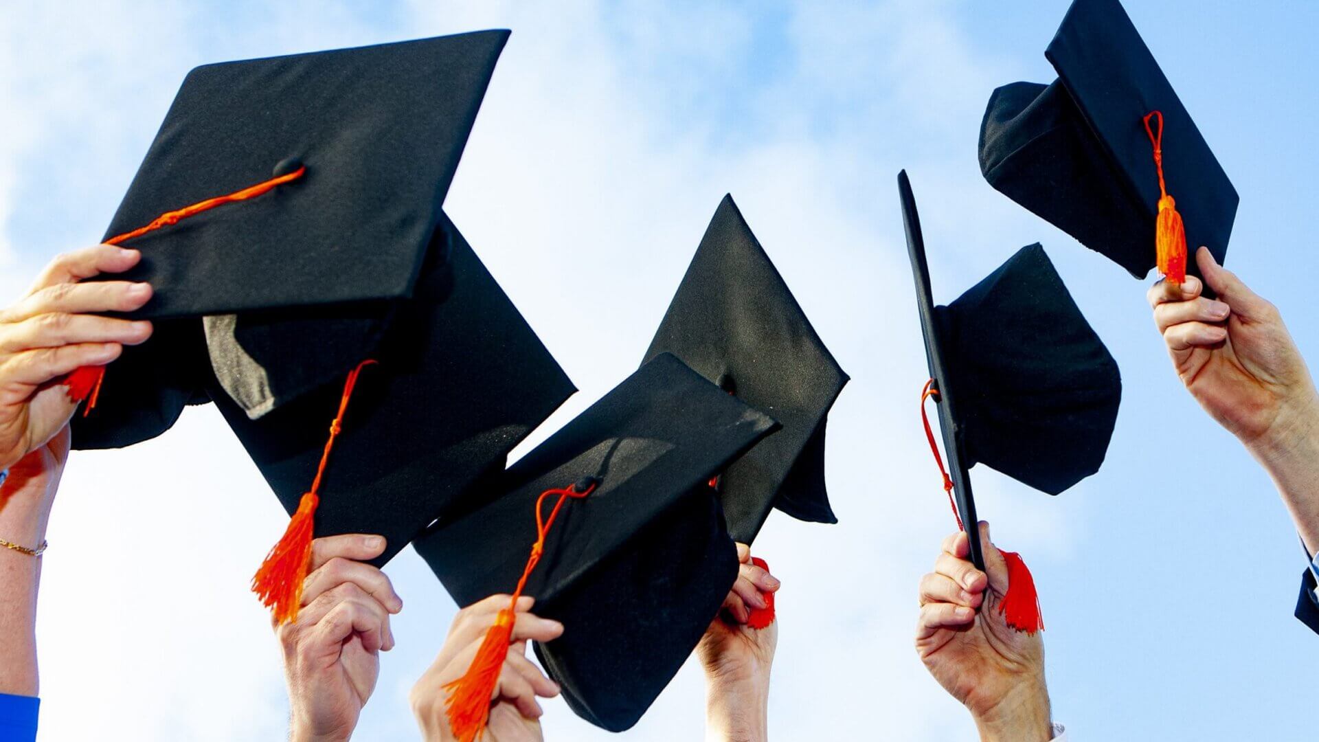 six people holding black graduation caps in the air