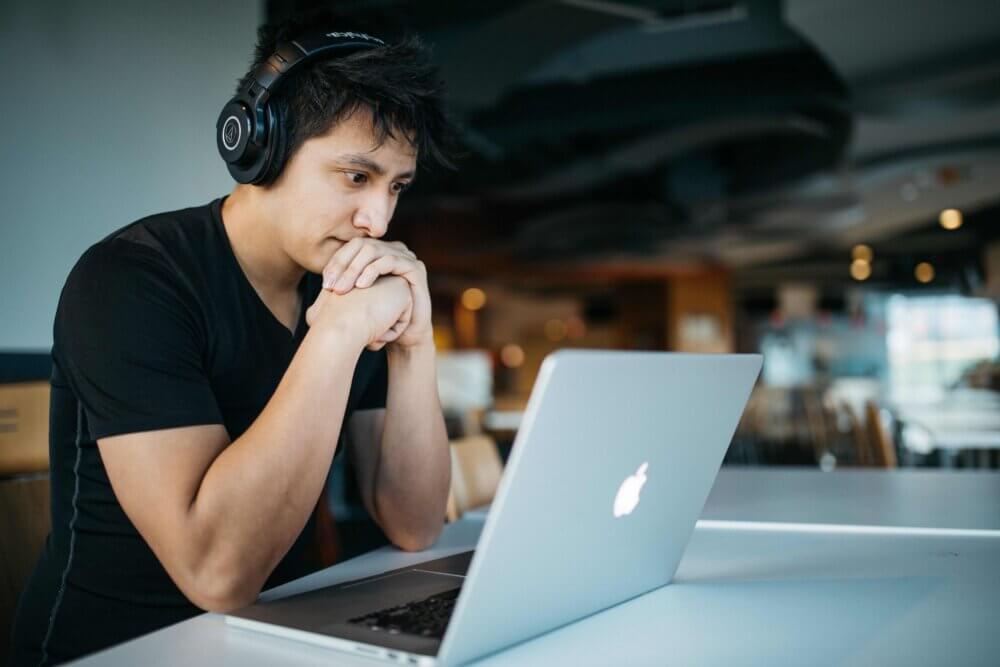 a man wearing headphones stares intently at his laptop screen