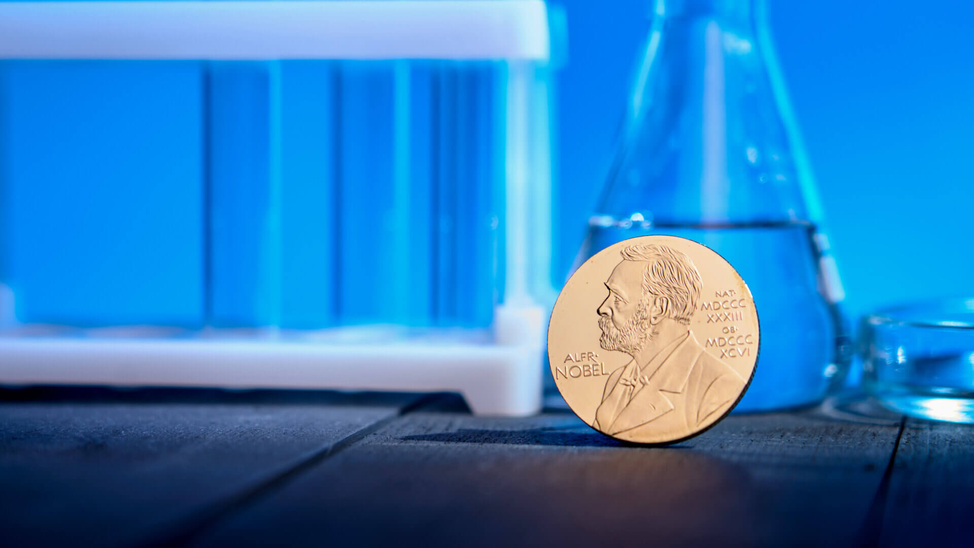 Nobel award against backdrop of chemical test tubes on blue background.