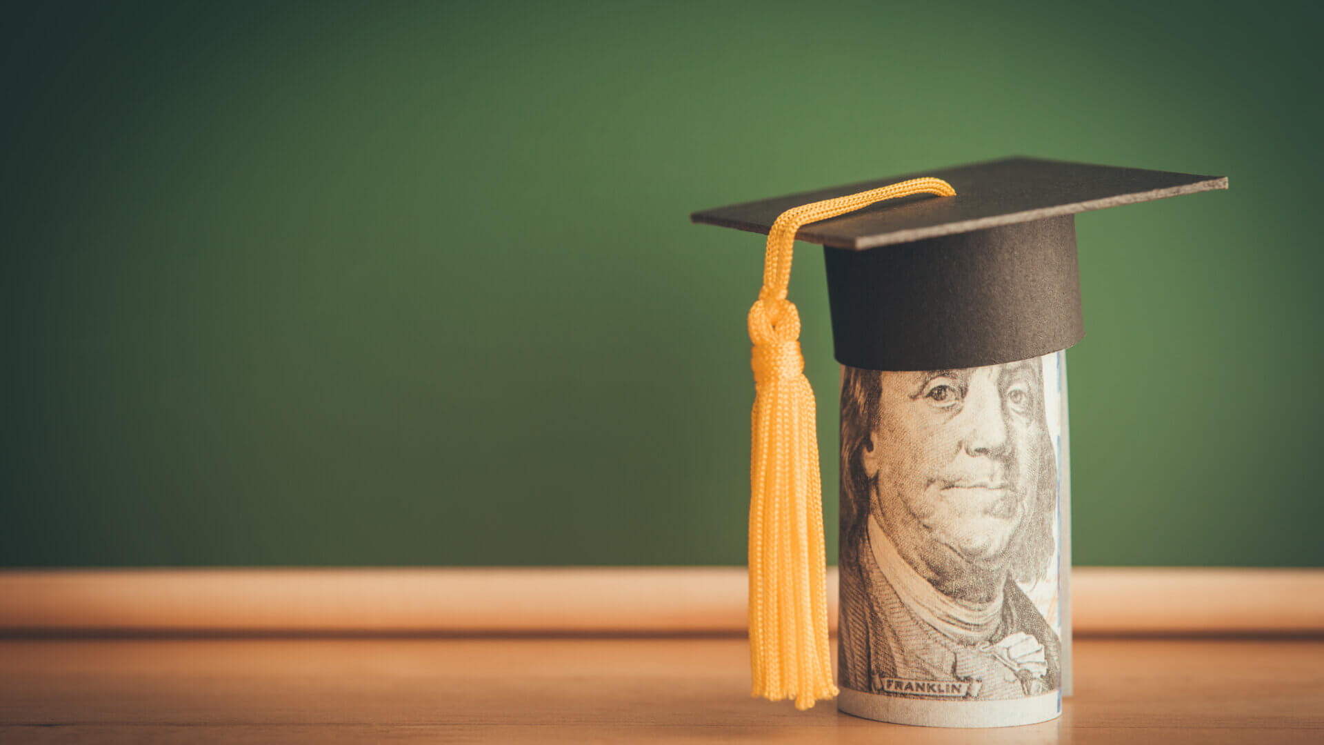 US dollars banknote wears graduation cap chalkboard background in classroom.