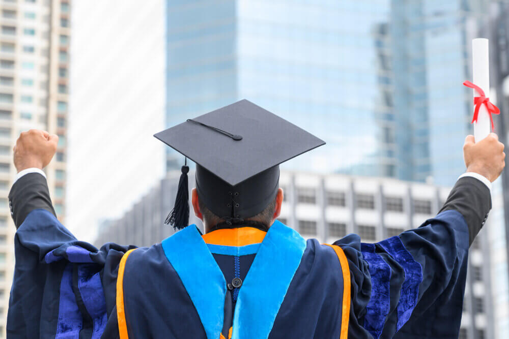 A man in graduation gowns holding diploma in hand on urban city background.