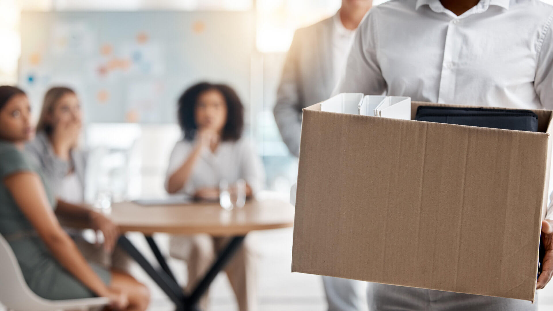 Employee laid off, walking away from office with box of belongings in arms.